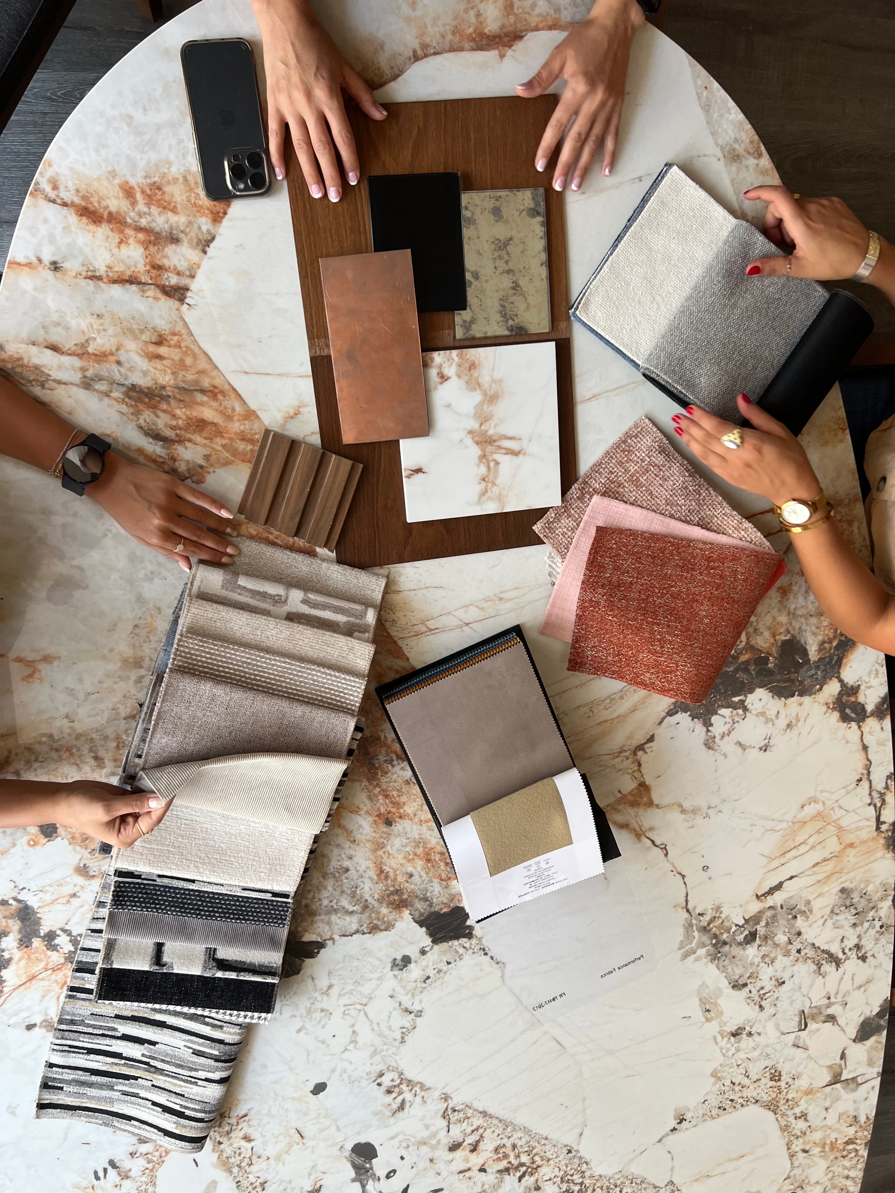 The Gallery LA studio selecting materials — fabric, marble, wood, and metal samples on a marble table